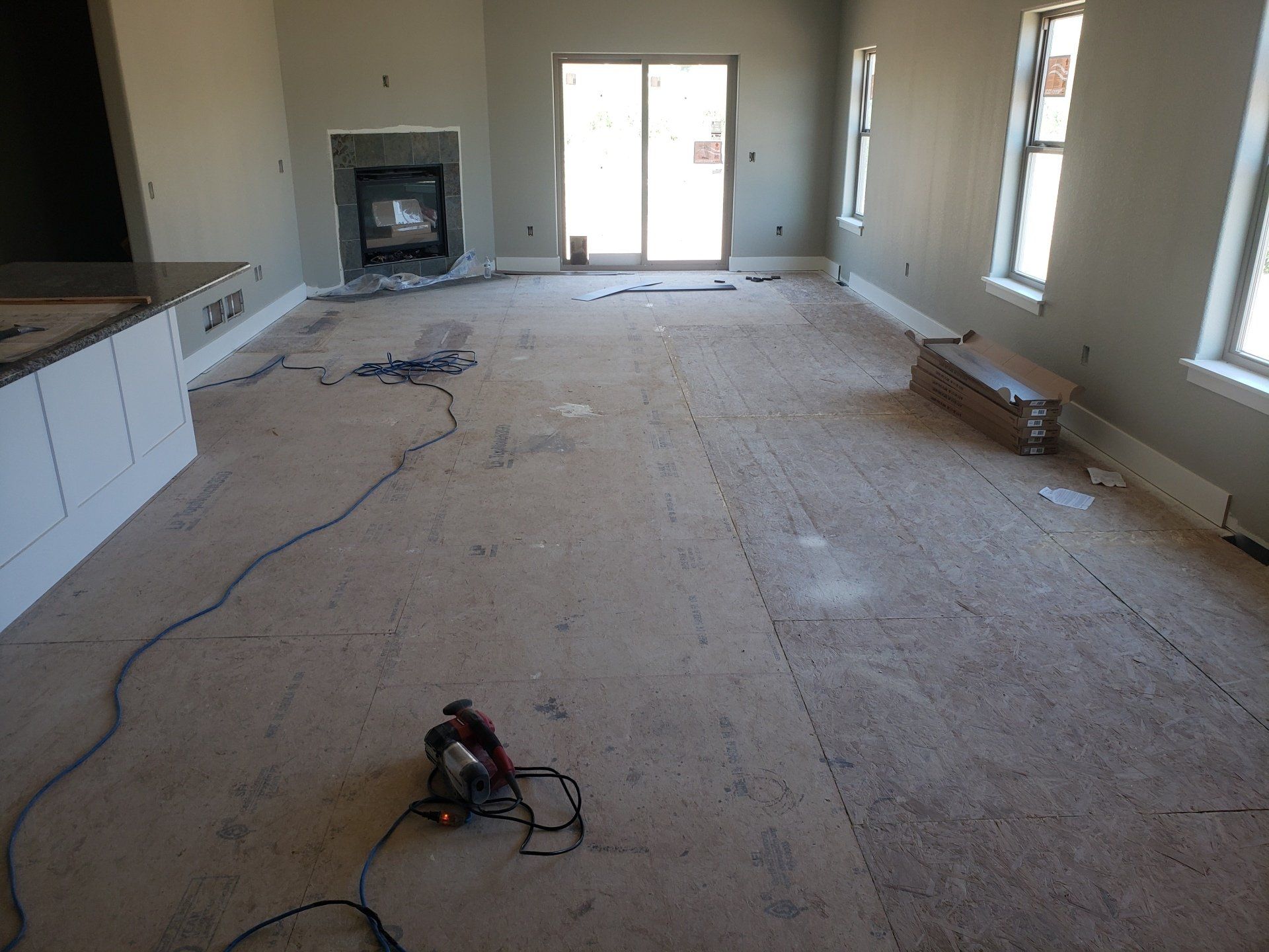 Empty room interior with fireplace, windows, and sliding glass door; subflooring and tools on the floor.