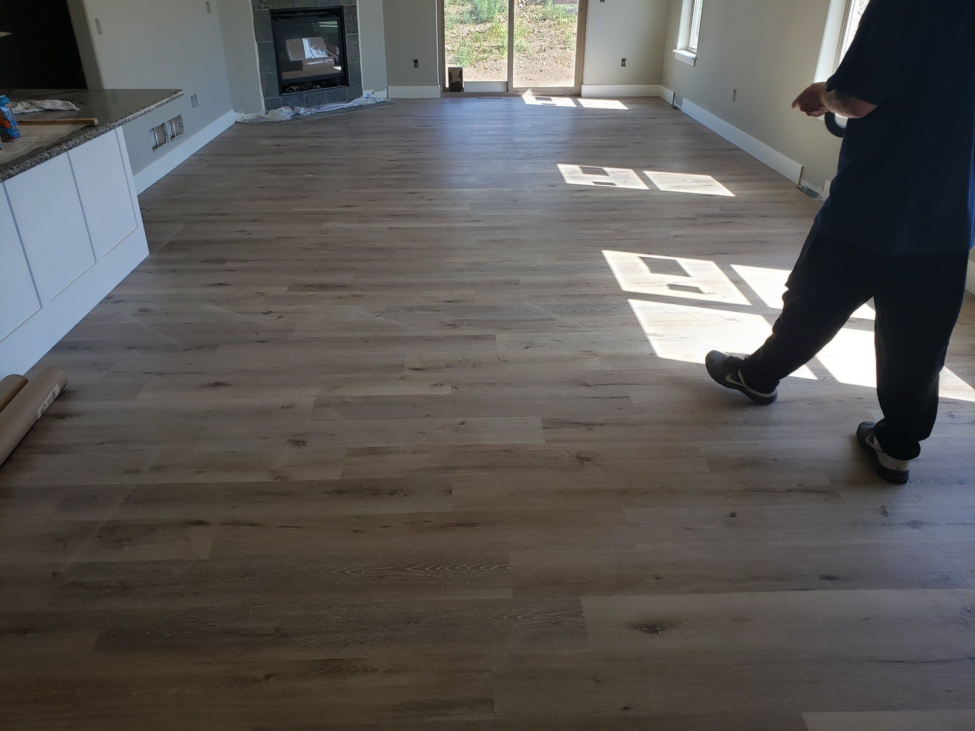Person standing on newly installed wood flooring in a room with a fireplace and large glass doors.