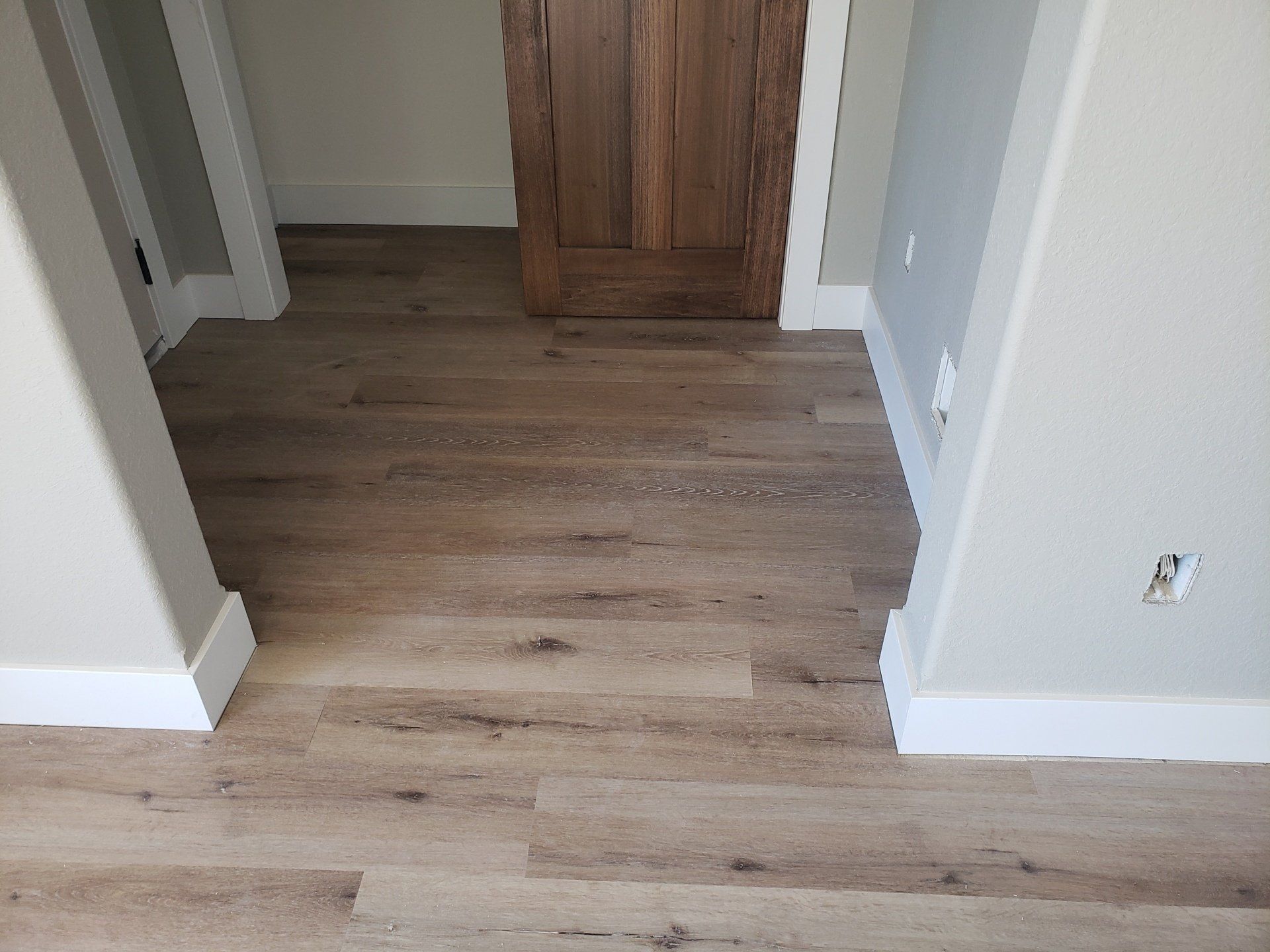 Light brown wood-look flooring in a room, with white trim and a brown wooden door in the background.