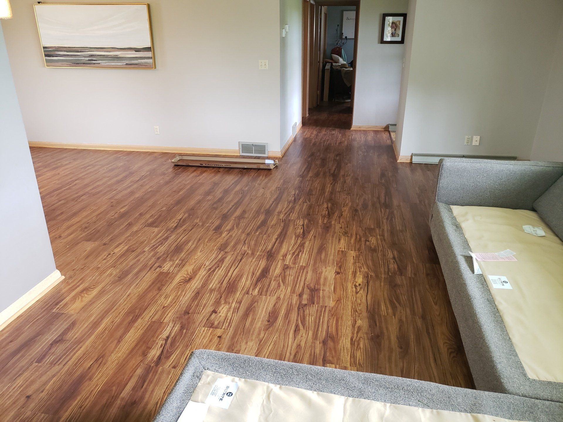 A room with wood-look flooring, gray walls, a framed painting, and a gray sectional sofa.