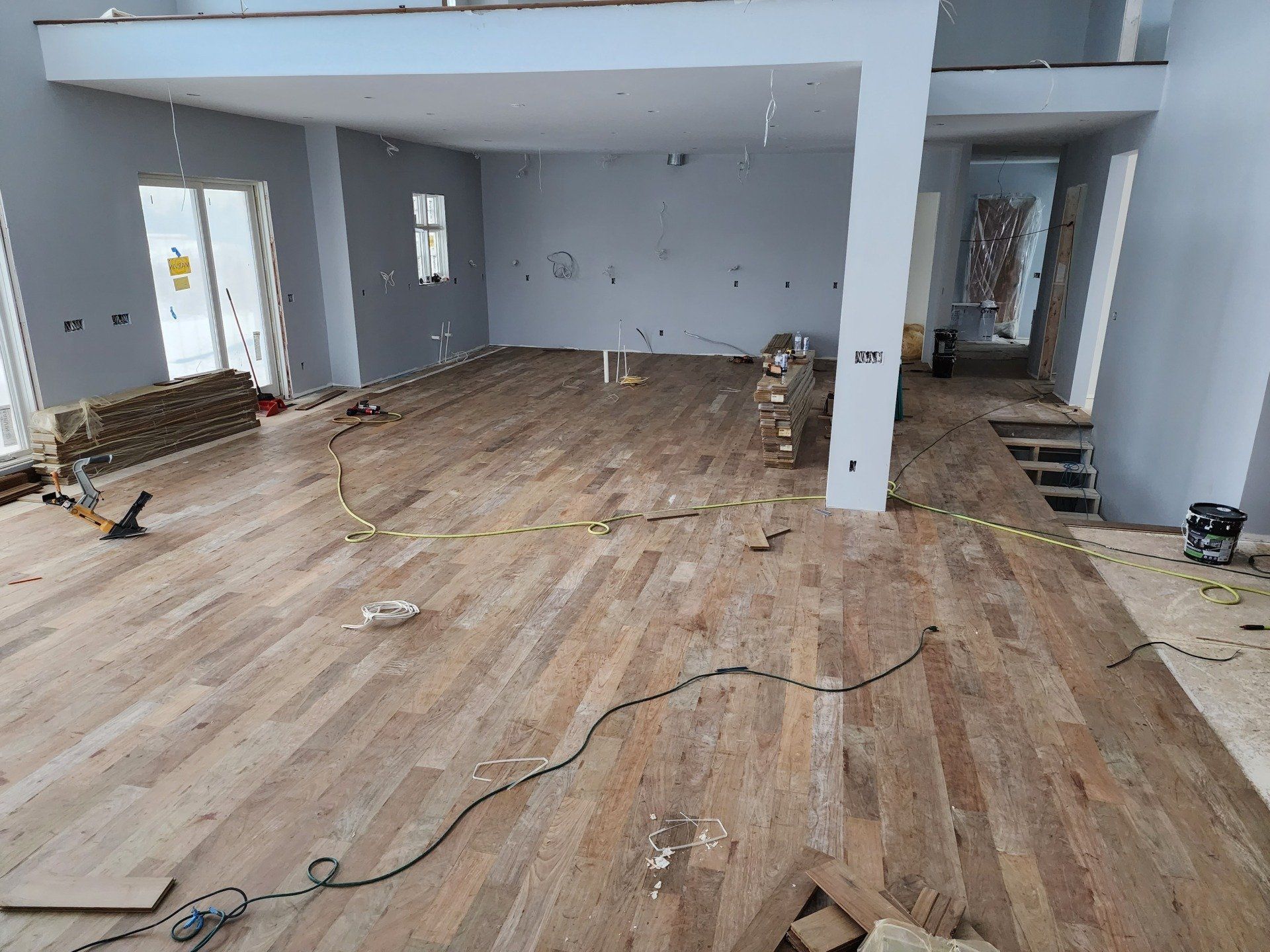 Wood flooring being installed in a light-colored, two-story room with high ceilings.