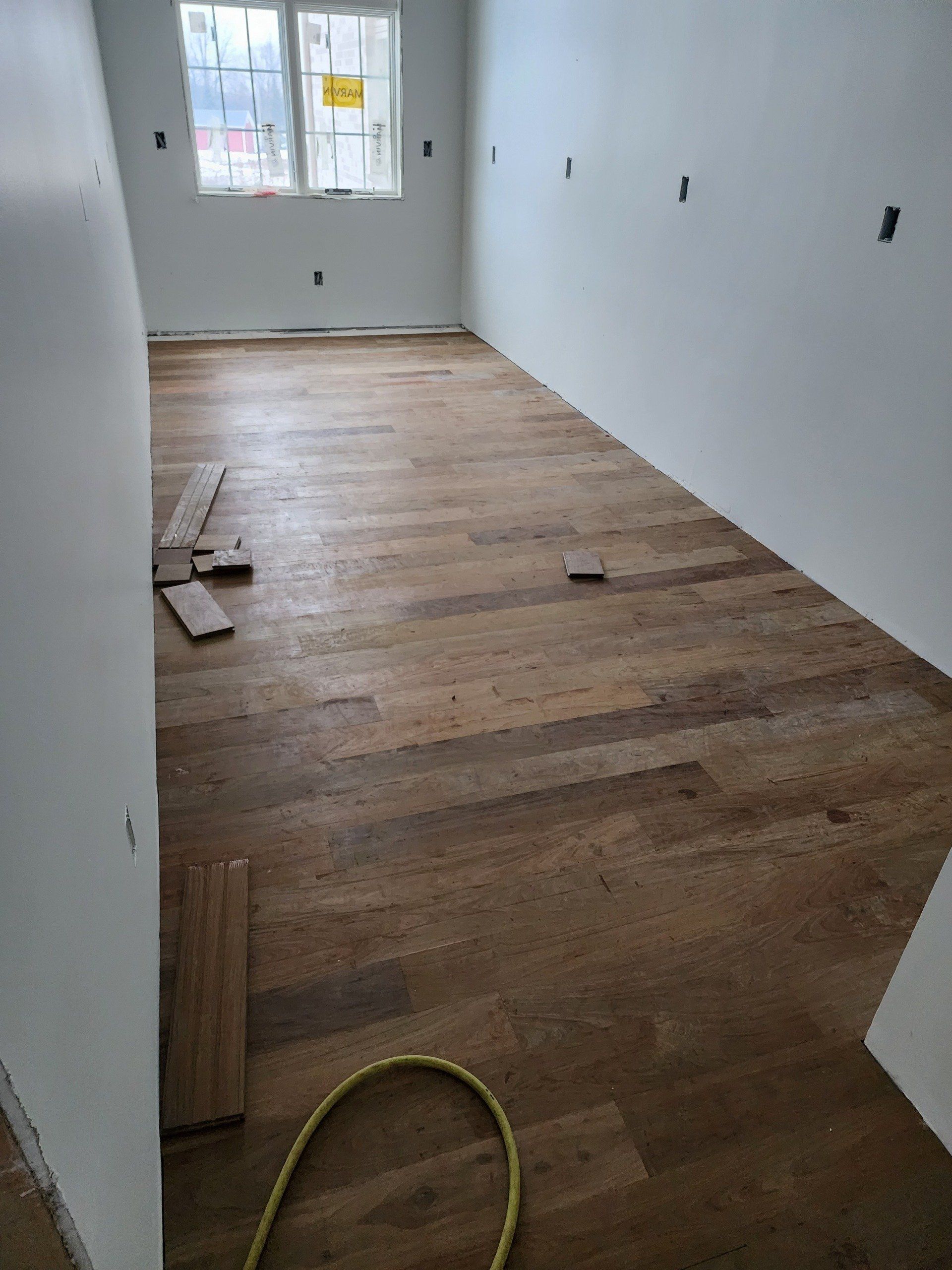 Room with unfinished wood floor, white walls, and a window. Construction in progress.