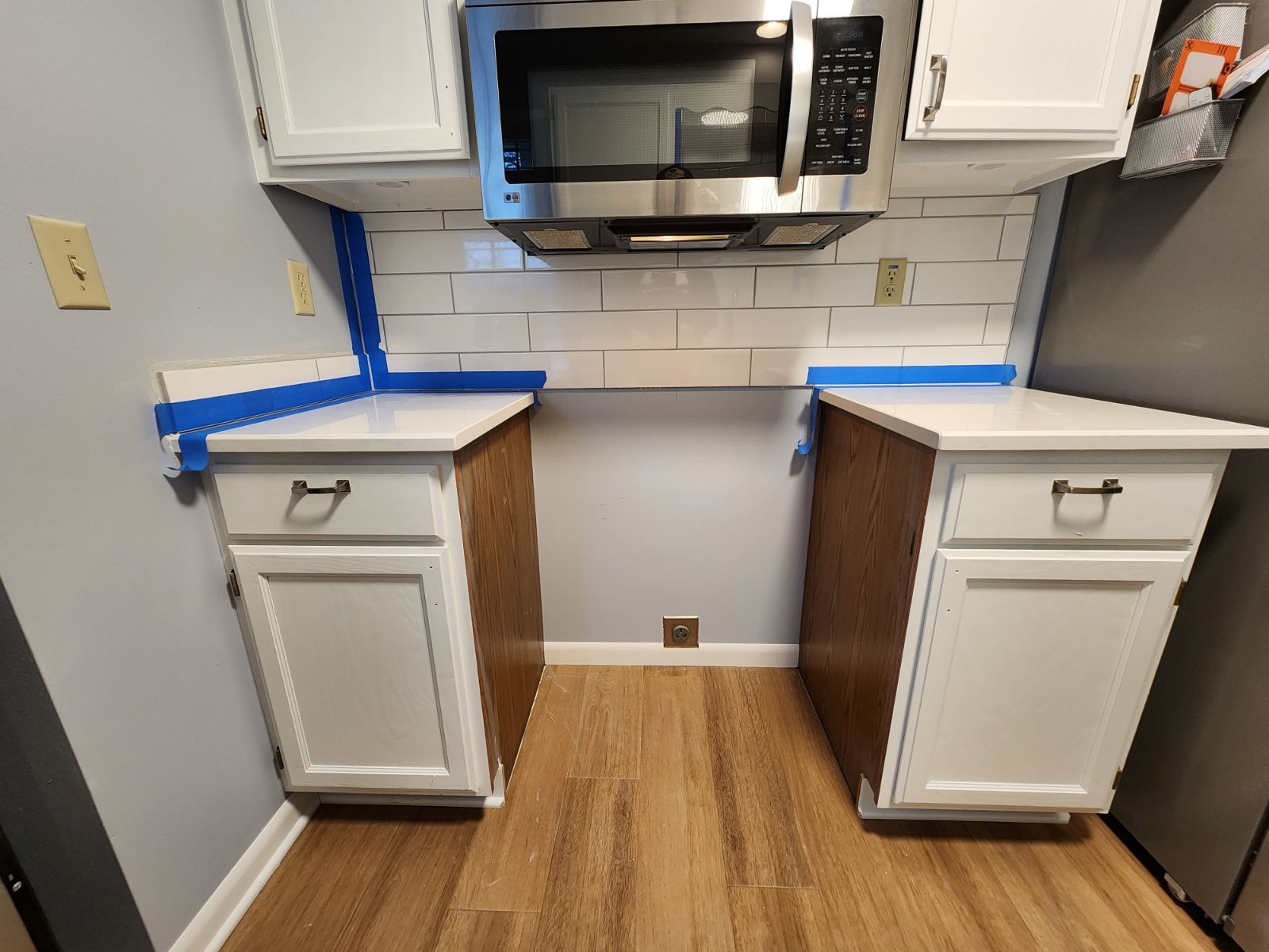 Kitchen remodel with white cabinets, white countertop, and subway tile backsplash. Brown cabinet sides.