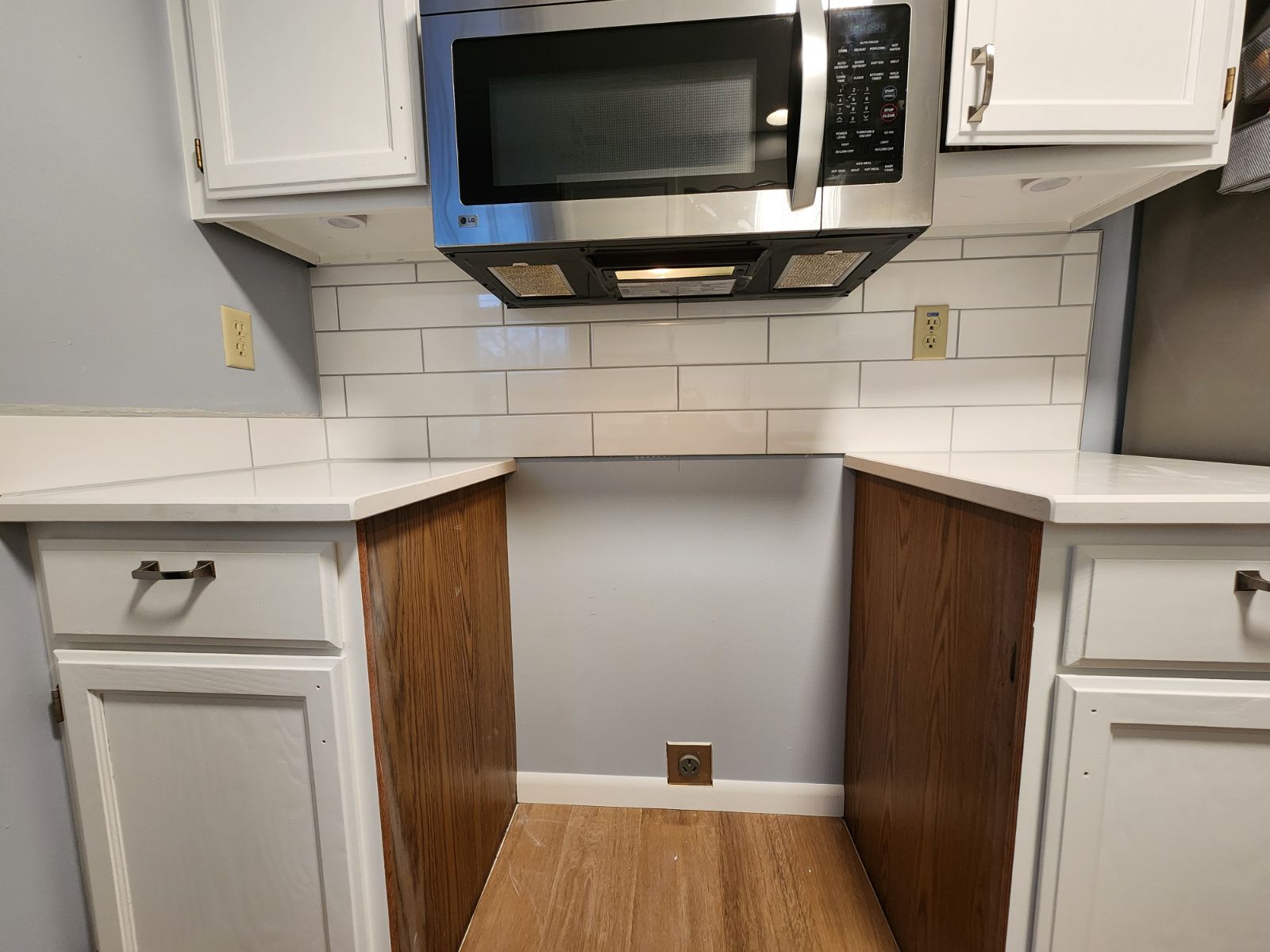 Kitchen with white cabinets, subway tile backsplash, stainless steel microwave and brown wood paneling.