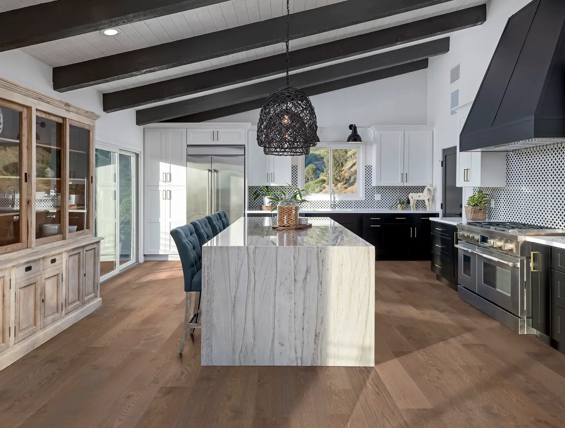 Spacious kitchen with light wood floor, white island, black and white cabinets, and dark ceiling beams.