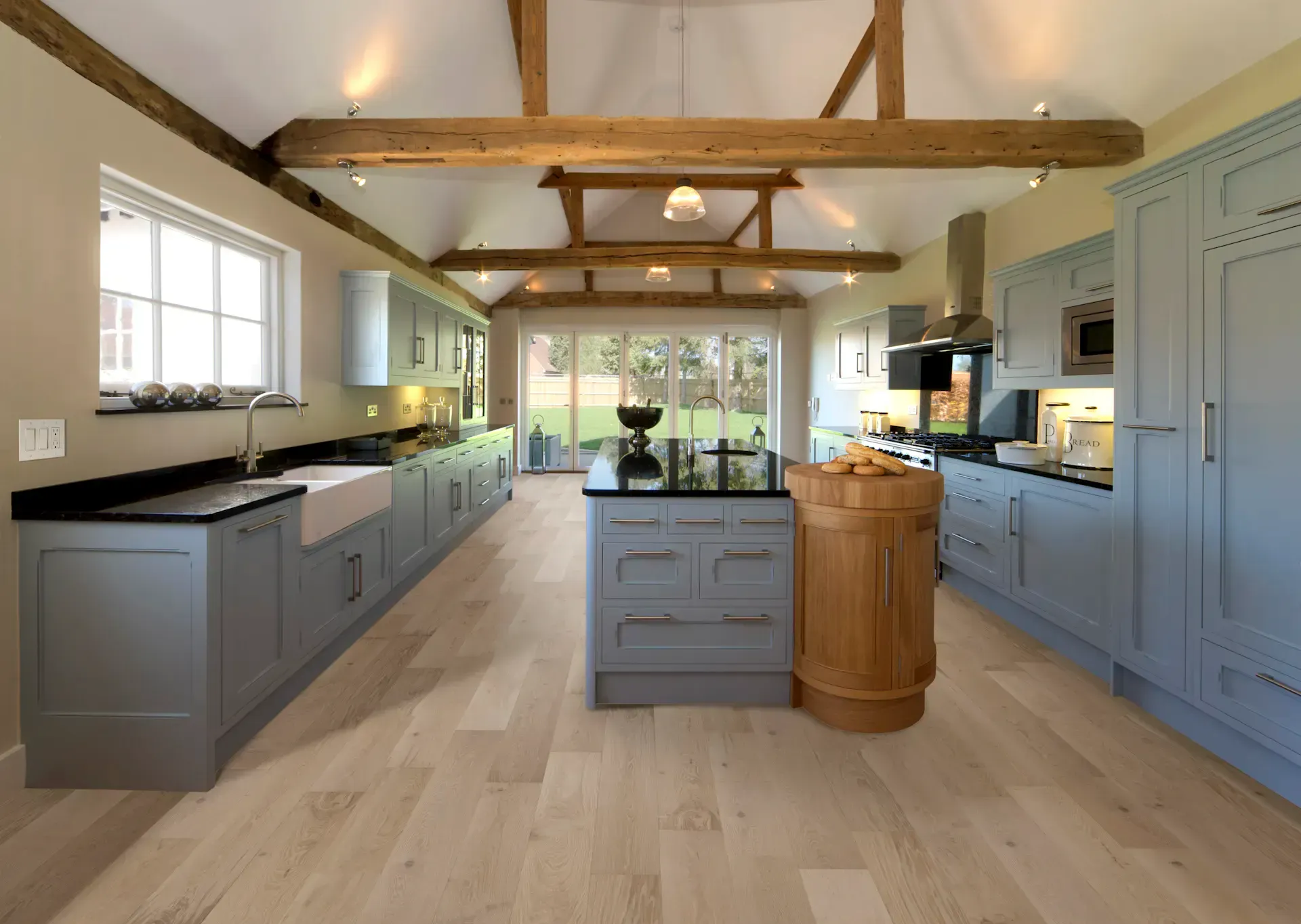 Spacious, modern kitchen with light blue cabinets, light wood floors, and exposed wooden beams.