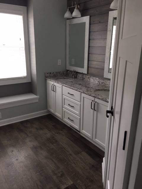 Bathroom with white cabinets, gray countertop, and wood-look floor. A large window and gray-washed wood accent wall.
