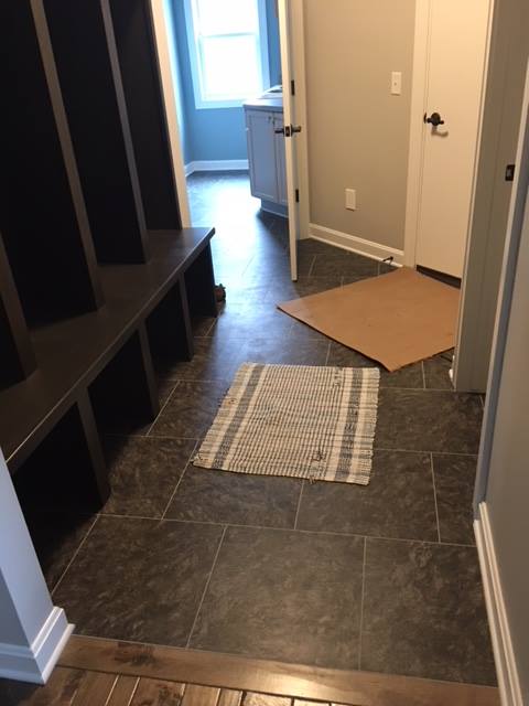 Entryway with dark tiled floor, built-in bench, door, and a rug. Brown and gray color scheme.