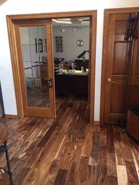 A doorway with wooden trim and a glass door reveals an office with a desk and furniture; hardwood flooring.