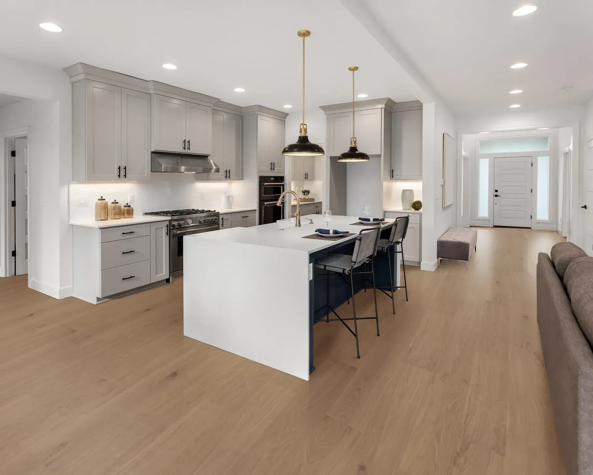 Modern kitchen with white island, gray cabinets, wood floors, and open to a hallway.