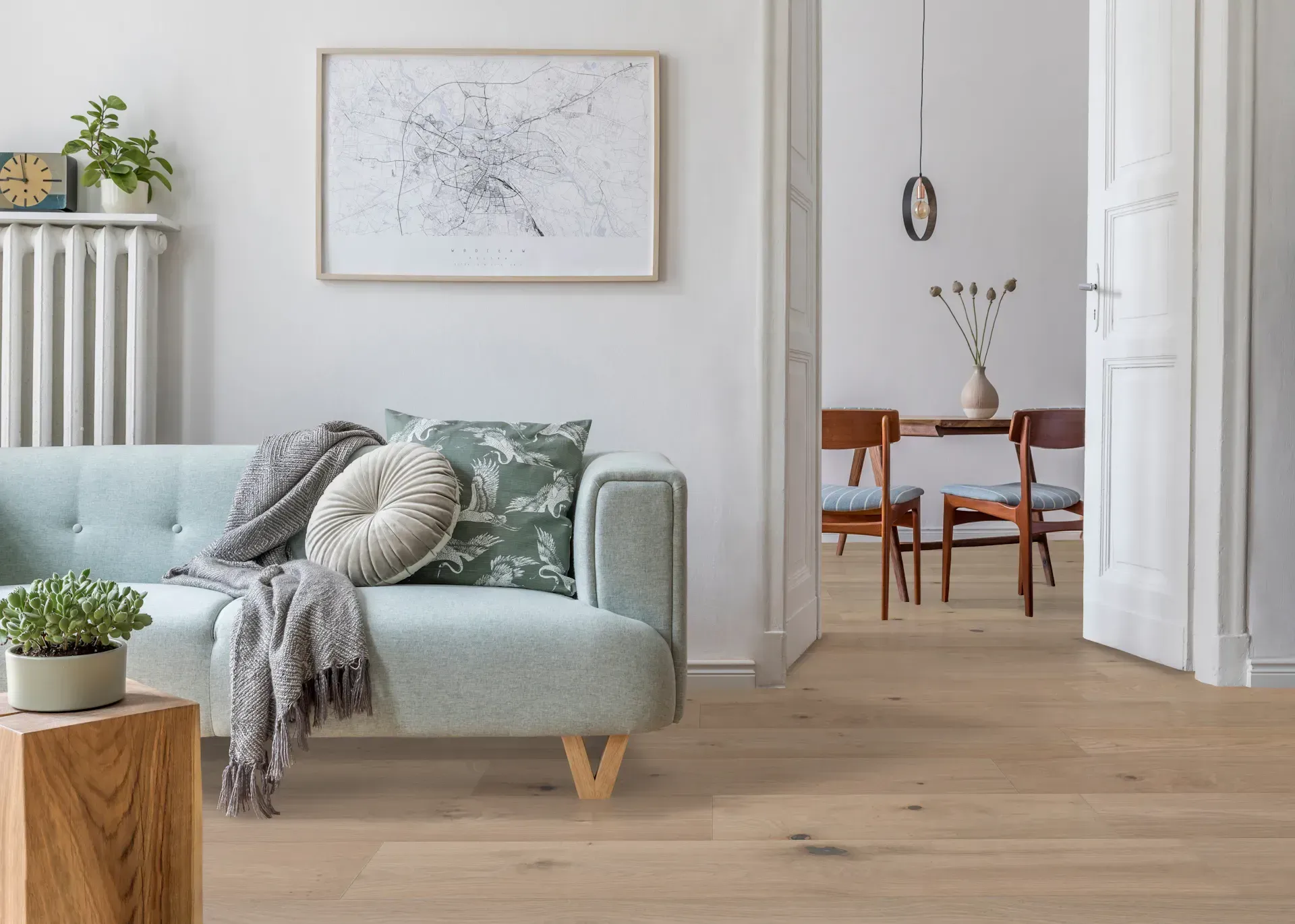 Living room with light blue sofa, art, and wooden floors. Door leads to dining area.
