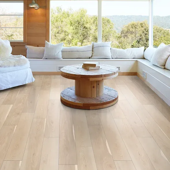 Light wood-floored living room with a wooden spool coffee table and a window seat overlooking trees.