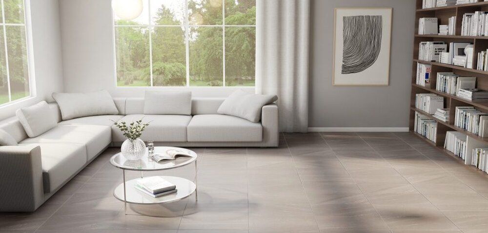 A bright living room with a white sectional, glass coffee table, and a bookshelf against a gray wall.