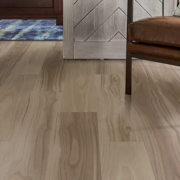 Wooden floor with natural grain pattern, light brown and tan tones. Chair and doorway in background.