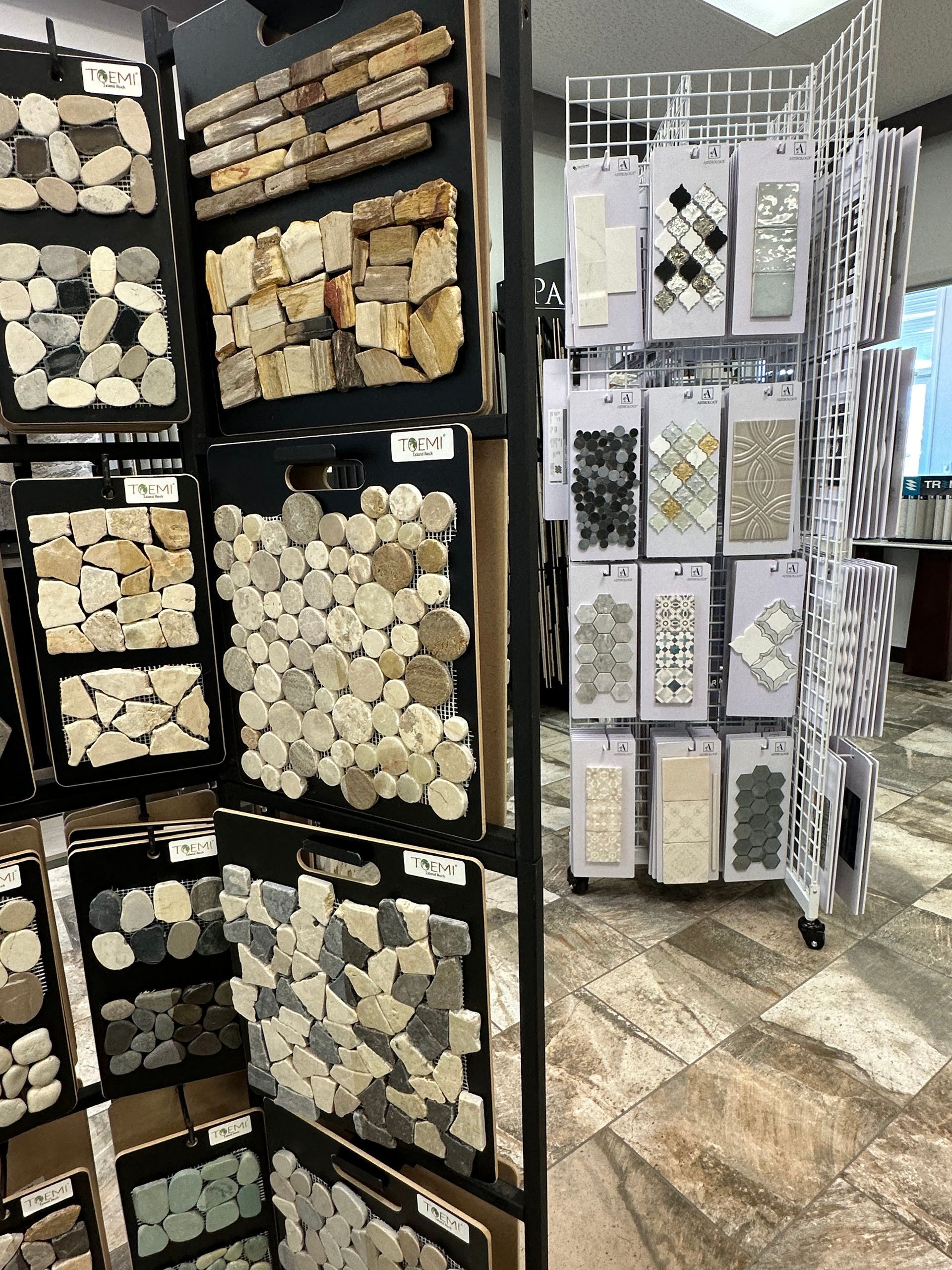 Display of tile samples on a multi-panel rack inside a showroom. Various tile types and colors are shown.