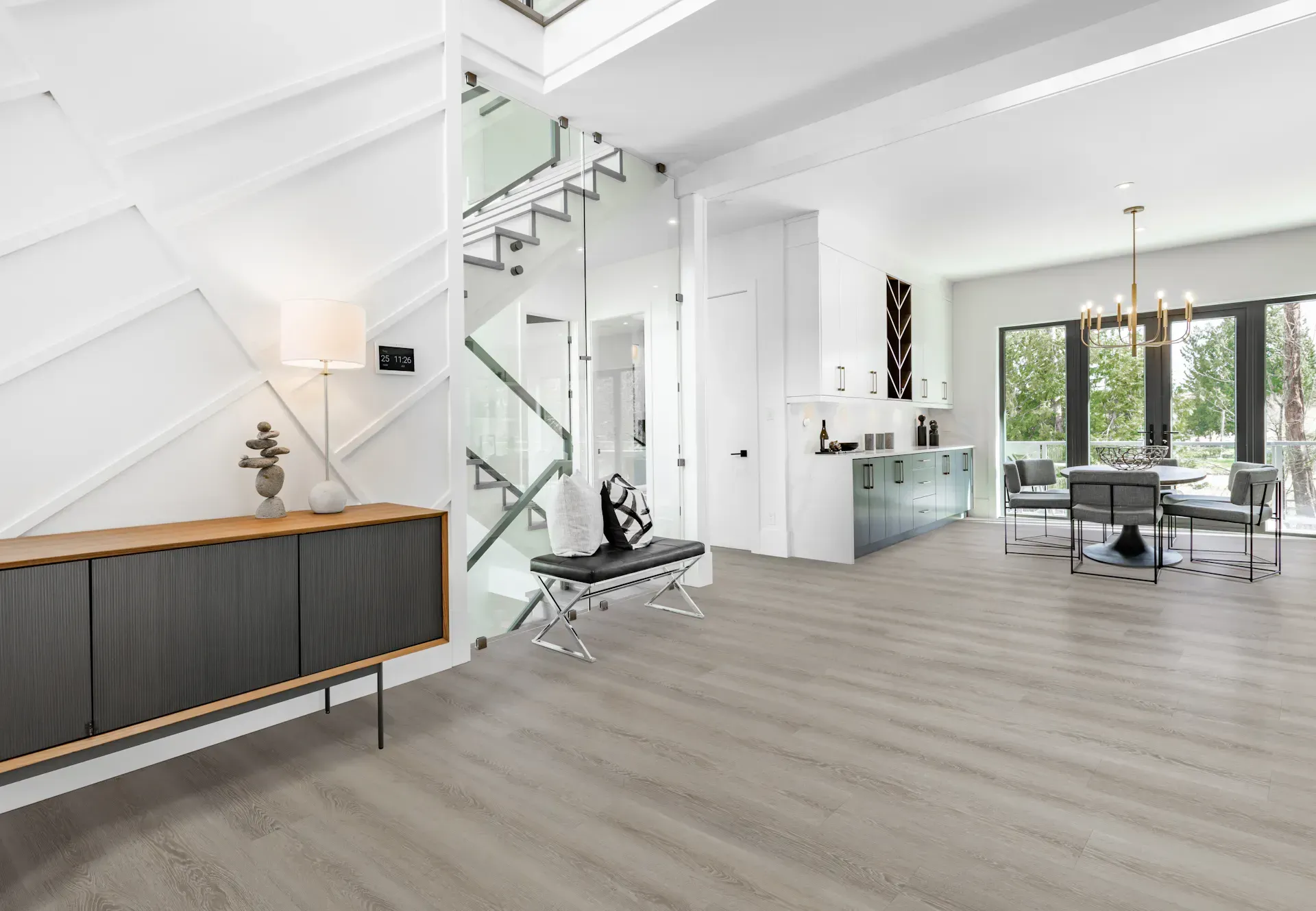Modern, bright interior with a staircase, dining area, and entryway. Light gray flooring, white walls, and glass railings.