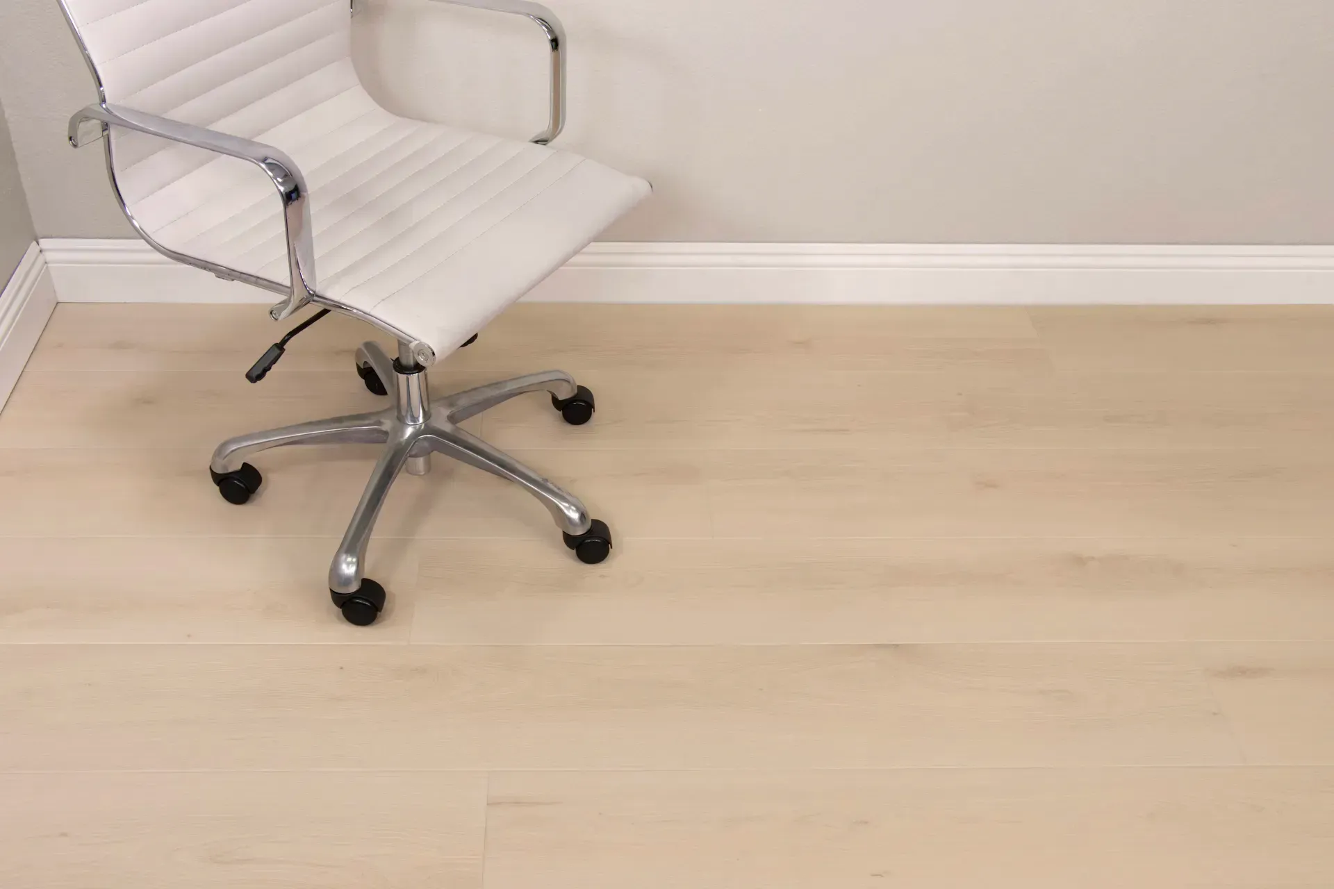 White office chair on light wood-look floor near a white baseboard and wall.