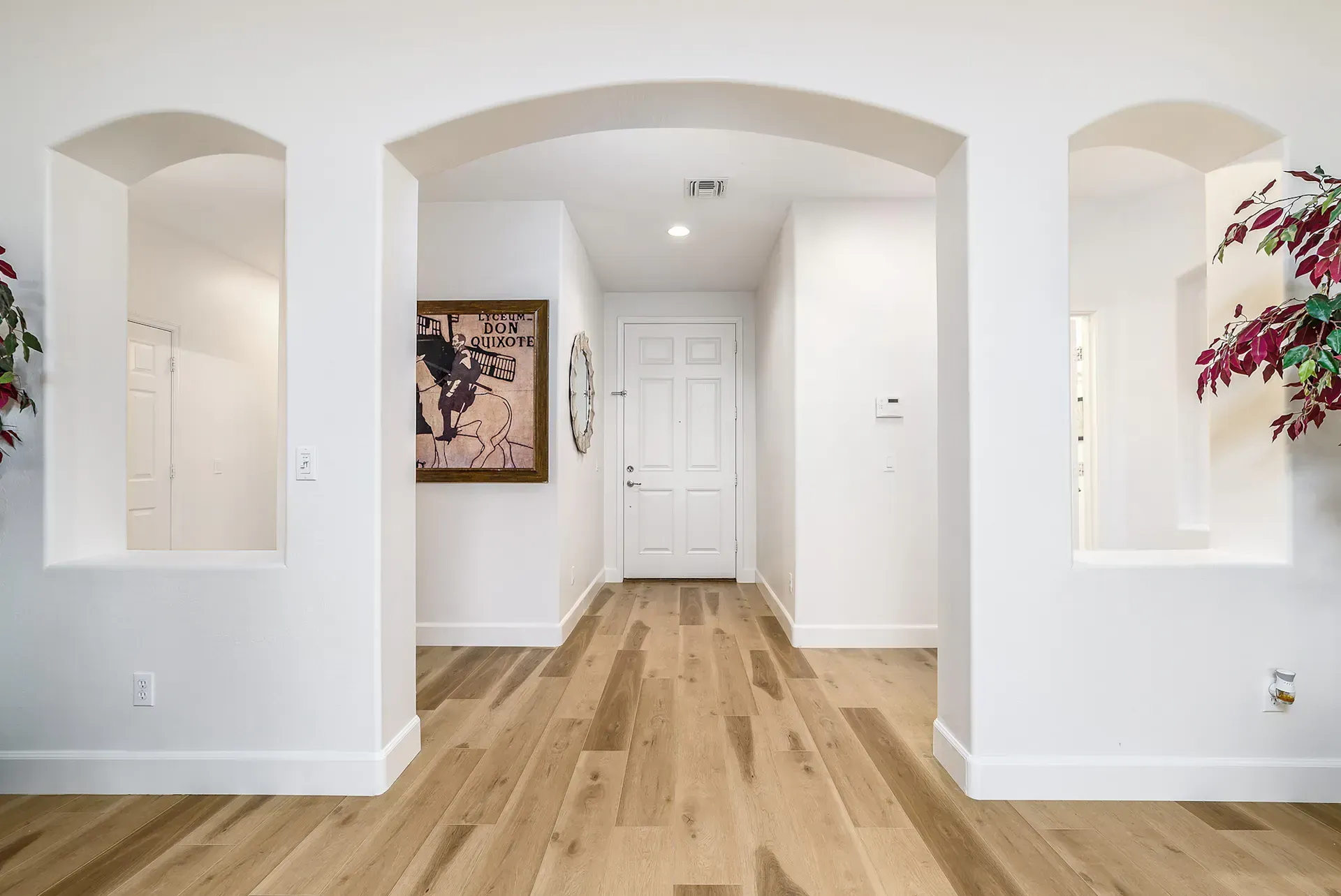 Hallway with arched doorway, light wood floors, white walls, and art.