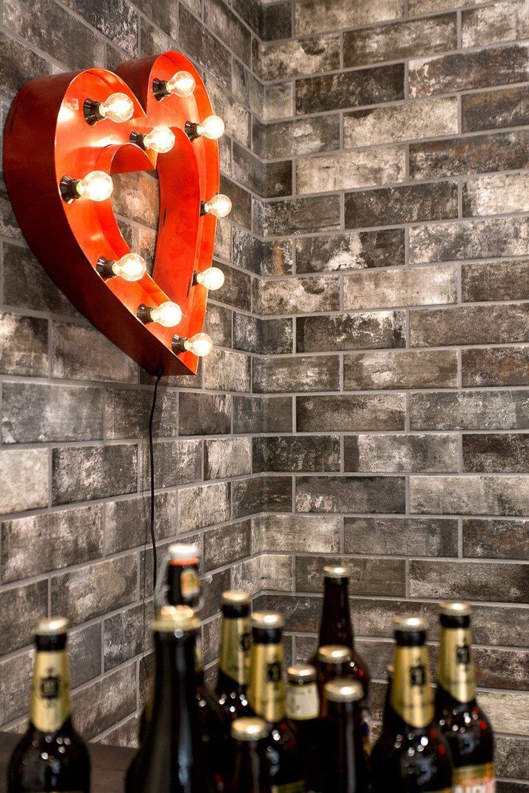 Red heart-shaped light fixture on brick wall, beer bottles below.