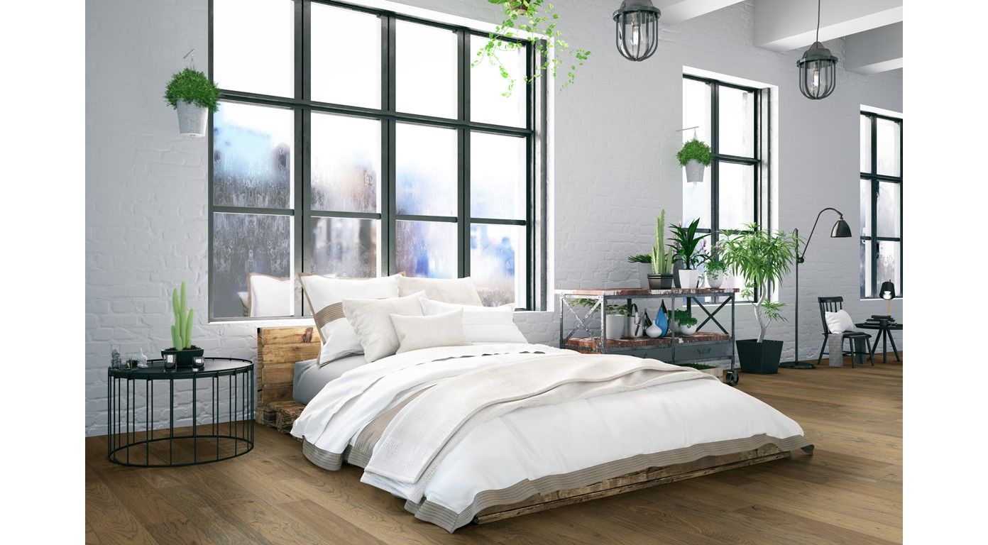 Bedroom with large windows, bed with white bedding, plants, and wooden floors.