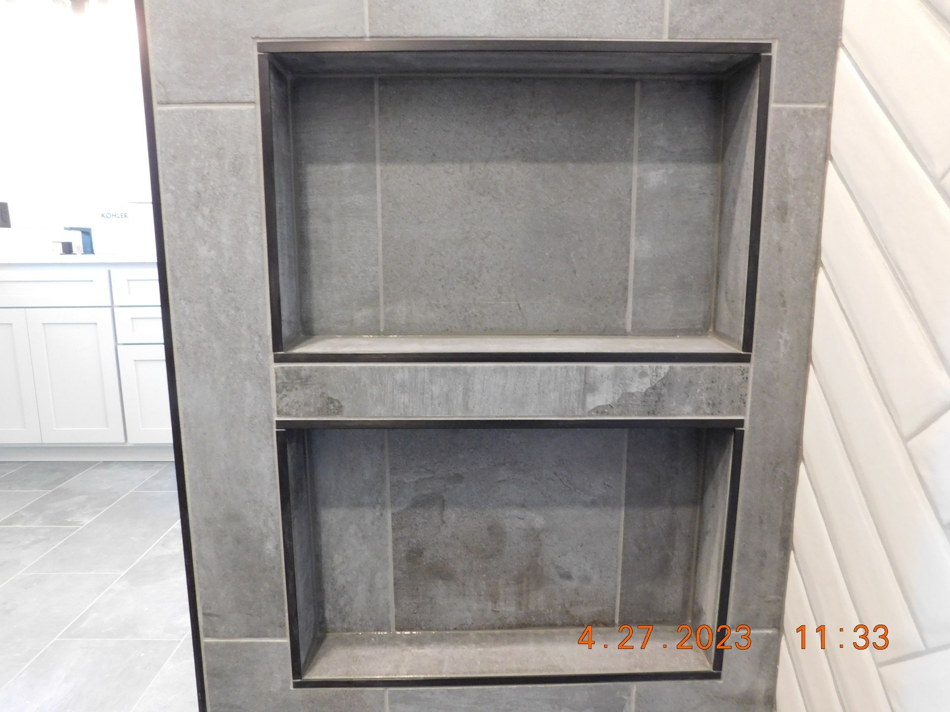 Two-tiered gray tiled shower shelf with dark trim, built into a wall.