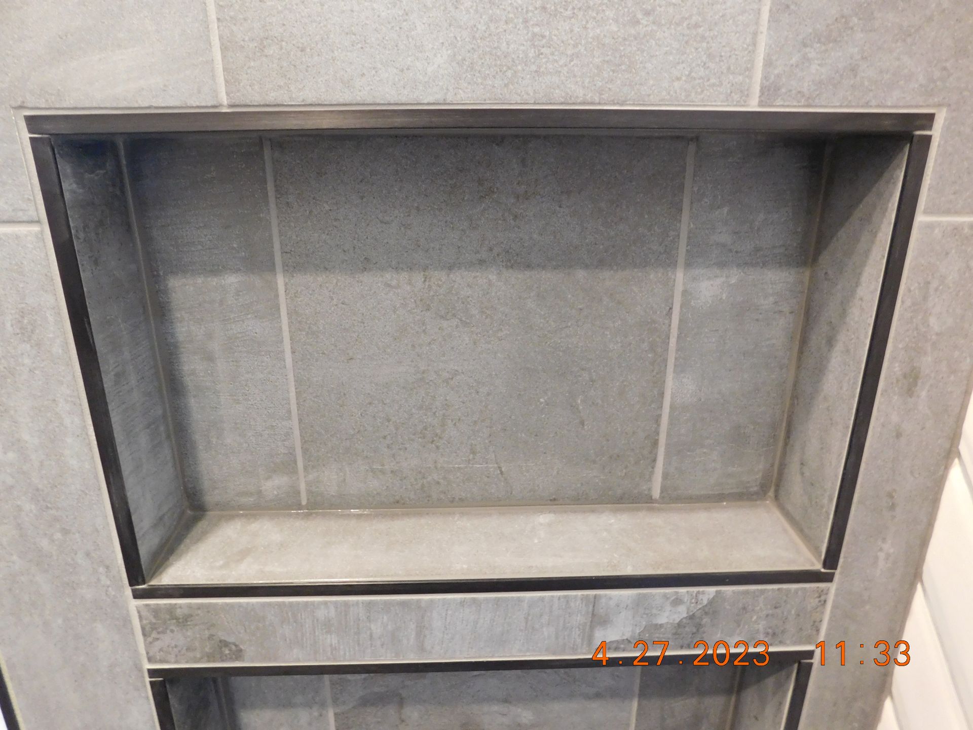 Recessed shower niche with gray tile and dark trim.