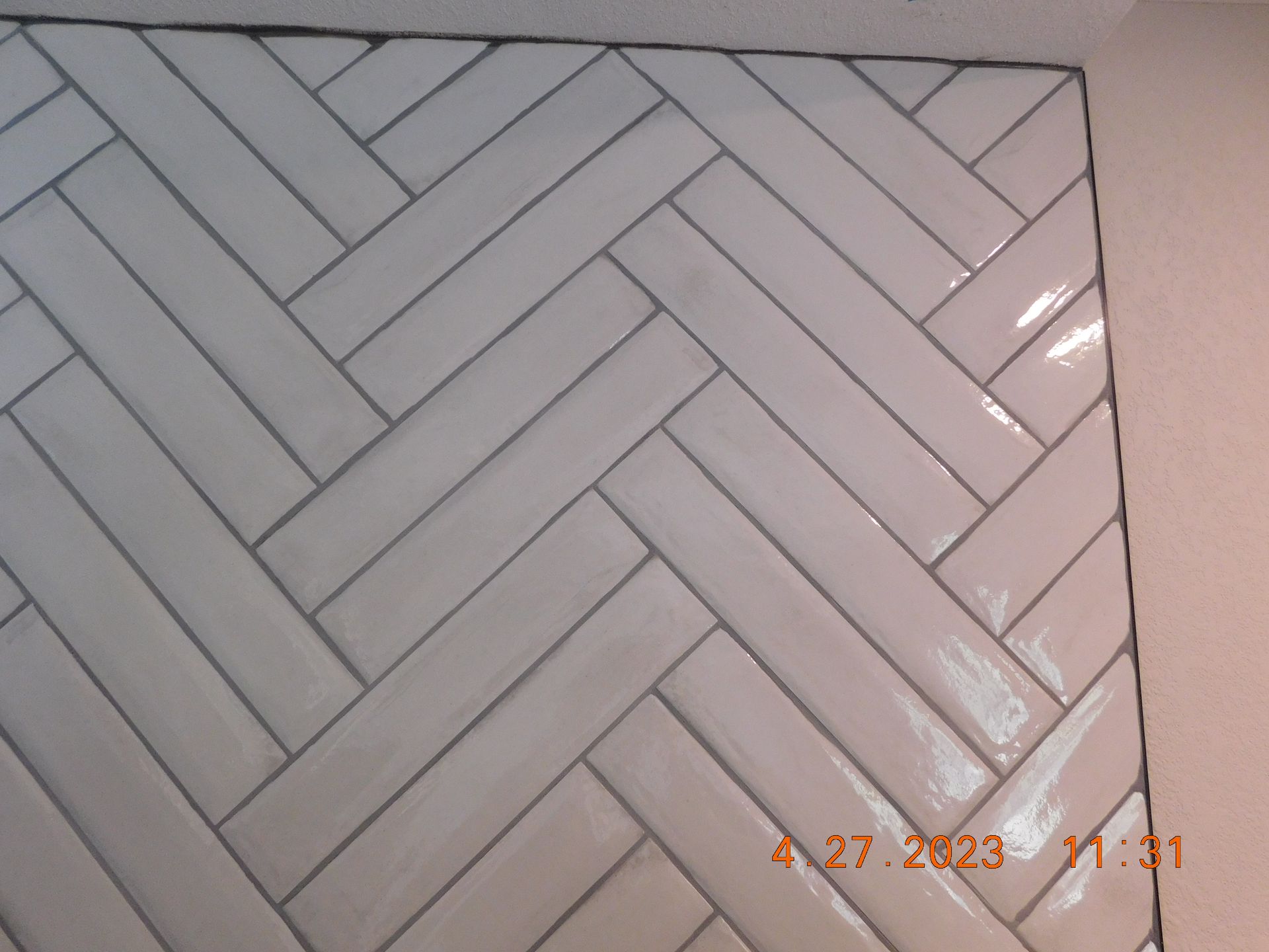 White, rectangular tiles arranged in a herringbone pattern on a wall. Dark grout lines.