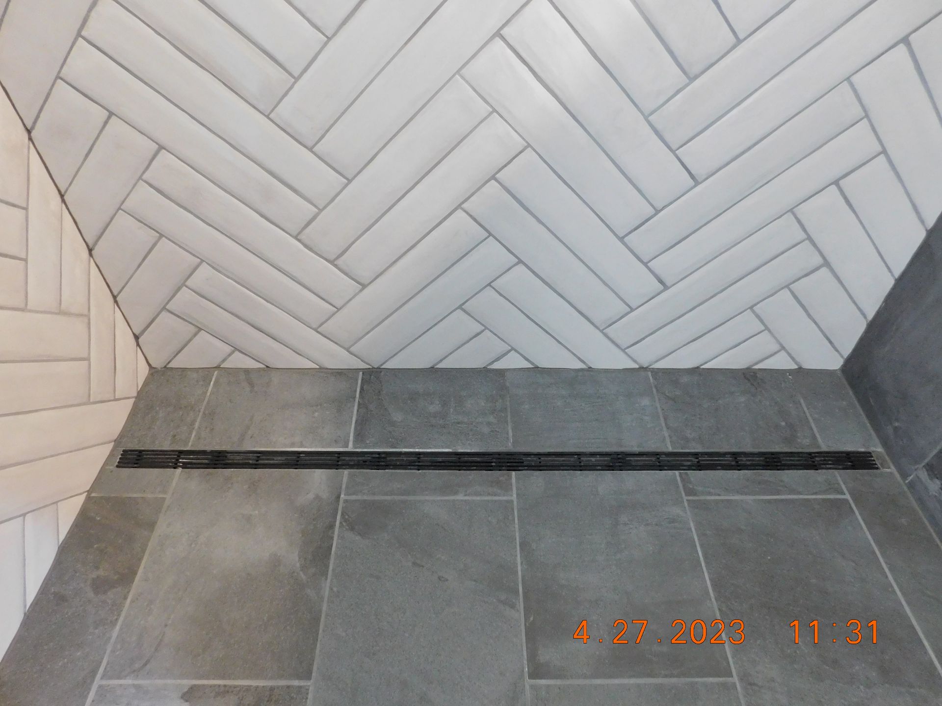 Shower with gray floor tiles, white herringbone ceiling tiles, and linear drain.