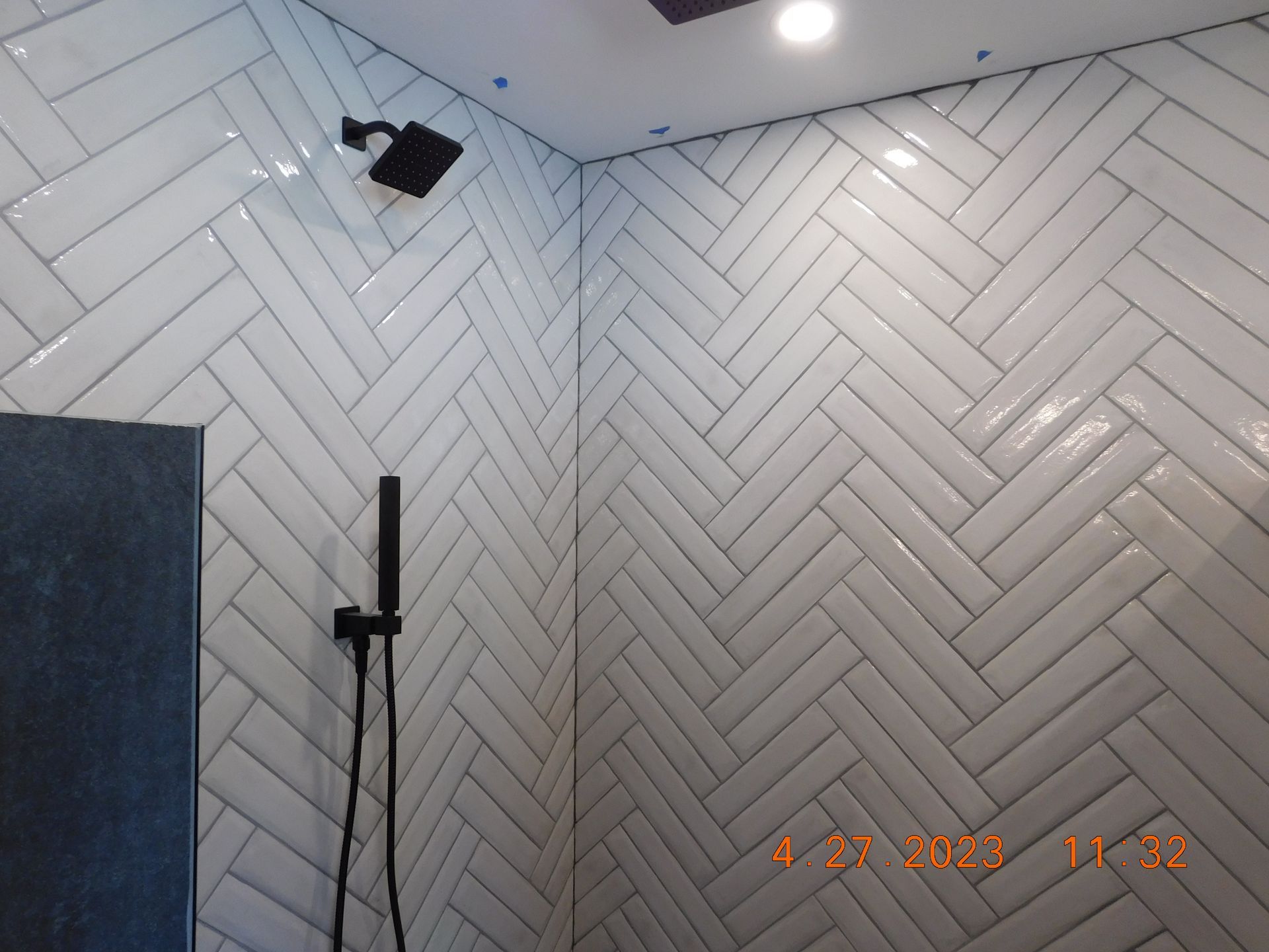 White herringbone tile shower with black fixtures.