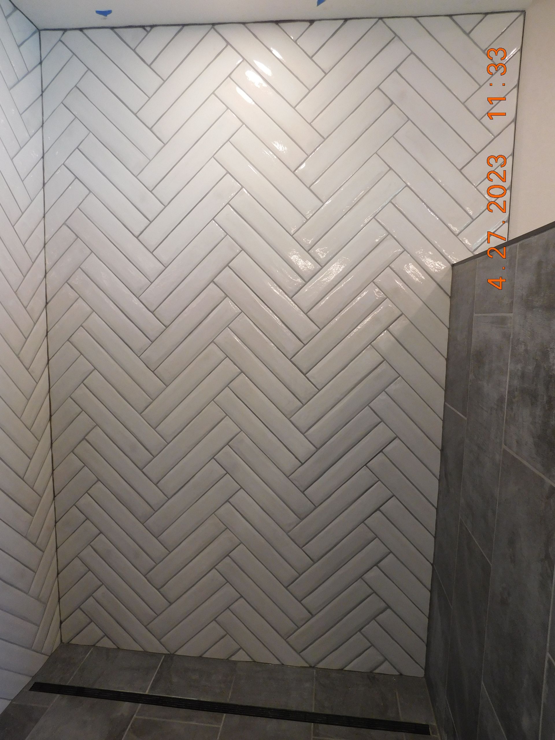 Herringbone-patterned white tile shower wall with gray floor and a dark gray side panel.