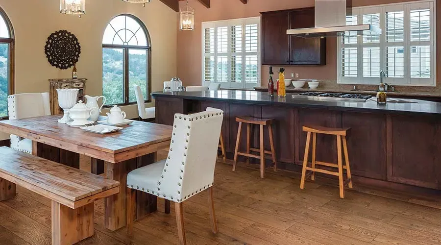 A rustic kitchen and dining room with dark wood cabinets, a large wooden table, and light wood floors.