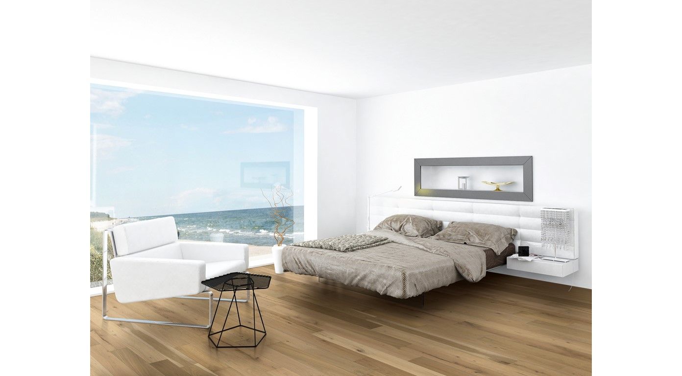 Modern bedroom with window overlooking ocean; white walls, wooden floor, bed with gray bedding, white armchair, black table.