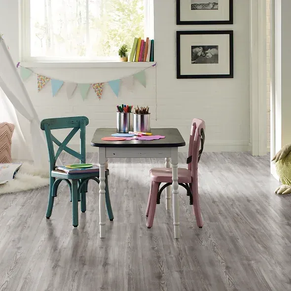 Children's play room with a small table and chairs, teepee, window, and books, with wood-look flooring.
