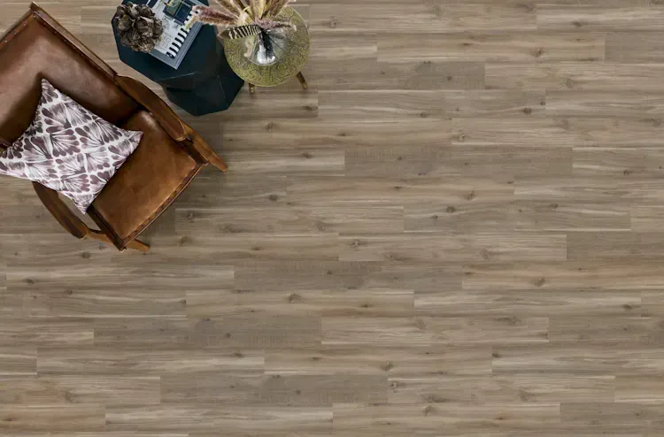 Overhead view of a brown wooden floor with a leather chair, throw pillow, and a small table.
