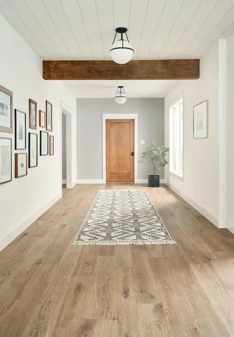 Hallway with wood floor, gray walls, art, and a patterned rug. Oak door at the end.