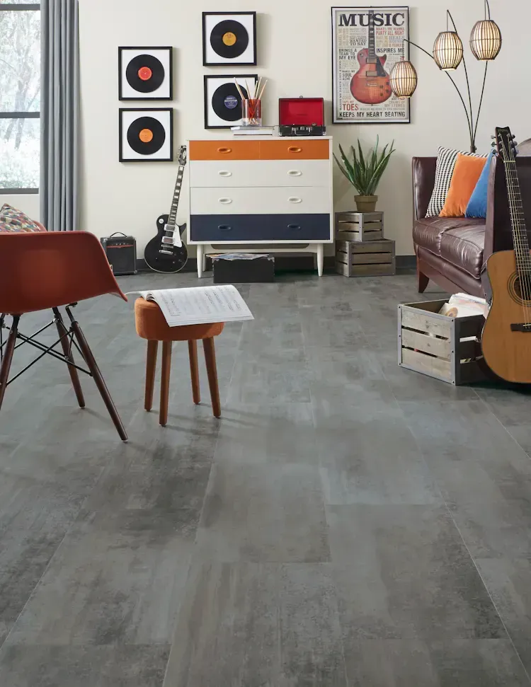Music-themed room with grey flooring, guitar, and record art; a brown leather sofa, and an orange chair.
