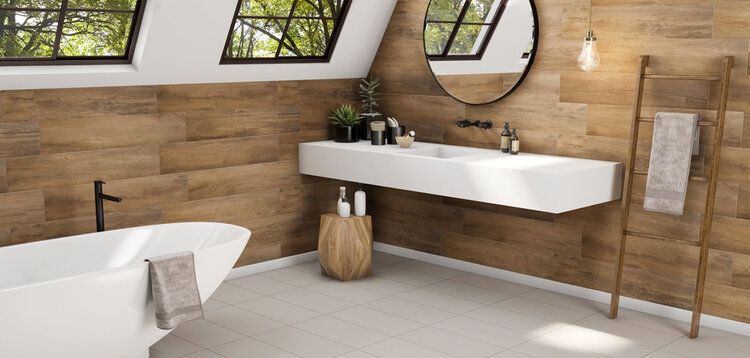Bathroom with wood-paneled walls, white bathtub, floating sink, and round mirror; natural light from windows.