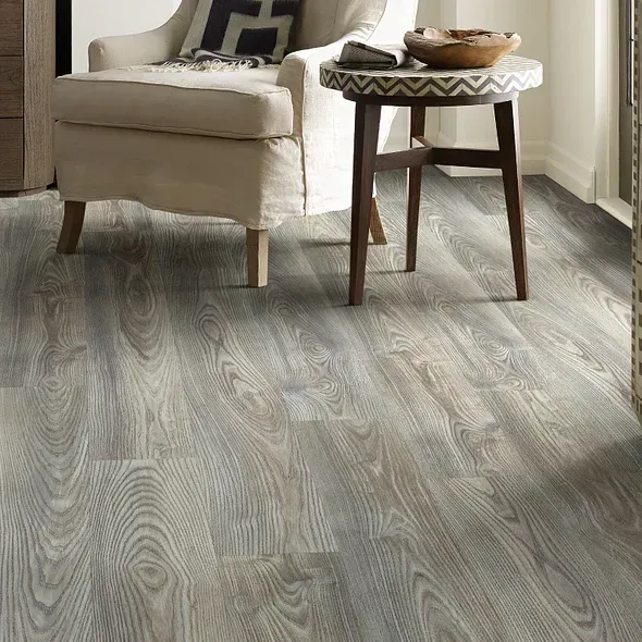 Gray wood-look flooring in a living room with an armchair and side table.