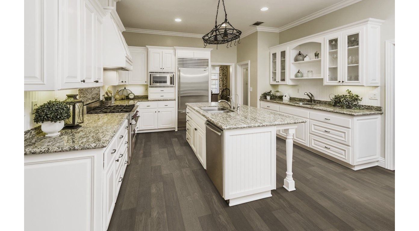 White kitchen with gray wood floor, white cabinets, and granite countertops. Island with a sink.