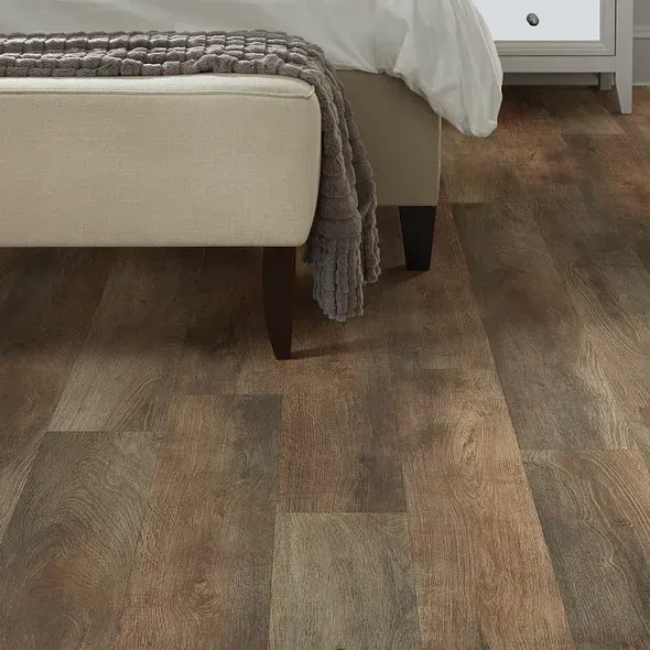 Brown wood-look flooring under a beige bench and bed.