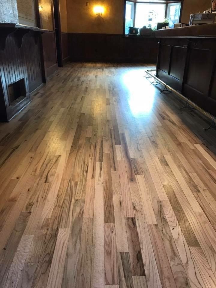 Wooden floor inside a bar, reflecting natural light. Dark wooden bar and trim frame the floor.