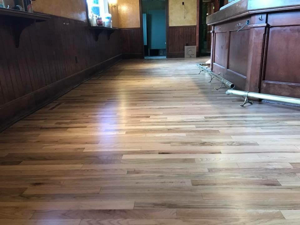 Wooden floor in a bar with brown wood paneling, a bar counter, and a doorway in the background.