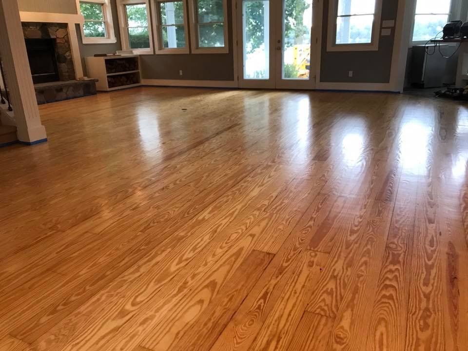 Polished hardwood floor in a bright room with natural light, reflecting the surrounding windows and doors.