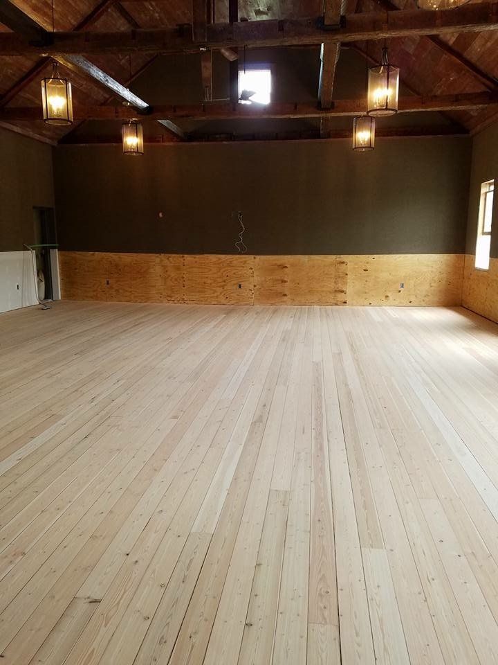 Newly installed wooden floor in a spacious, light-filled room with dark green upper walls and rustic wooden beams.