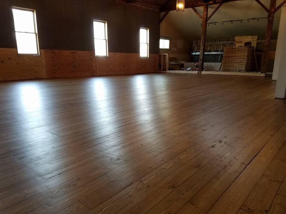Empty, spacious room with wood floor and several windows along the wall; natural light reflecting on the floor.