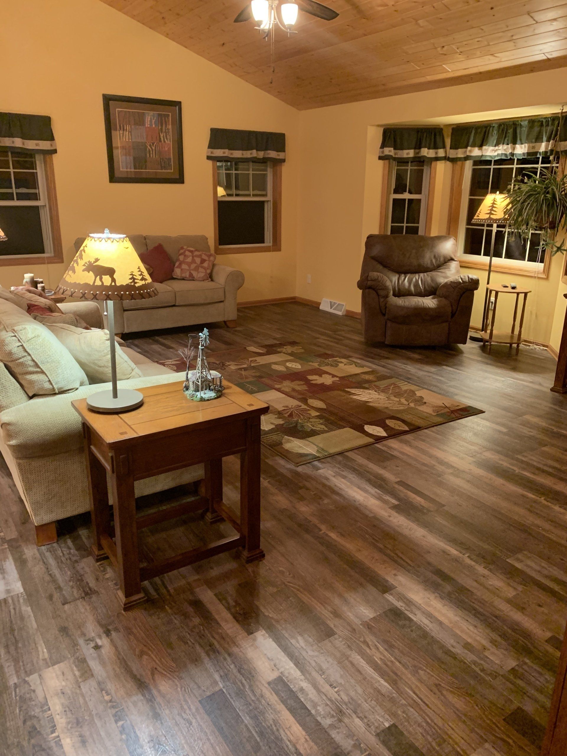Living room with wood-look floor, tan walls, couch, chair, windows, and rug.