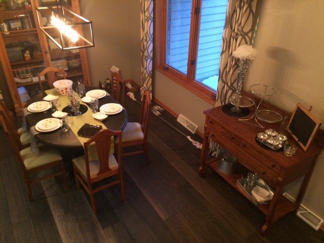 Dining room: round table set for a meal, buffet with serving dishes, wooden bookshelf, and window with curtains.