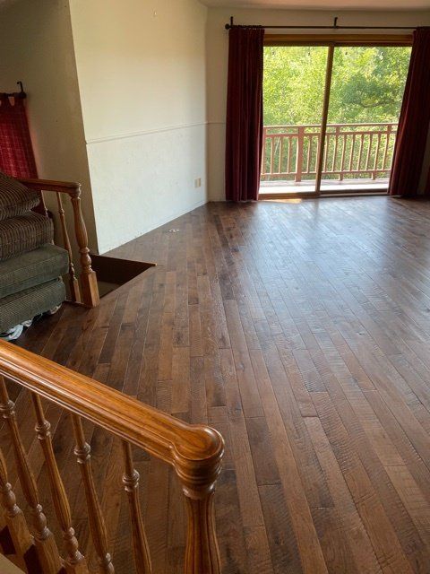 A living room with hardwood floors, a railing, and a sliding door to a balcony with red curtains.