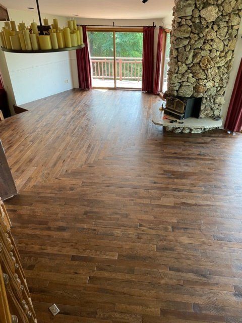 Wooden floor with a stone fireplace and sliding doors leading to a balcony. Red curtains and a chandelier are visible.