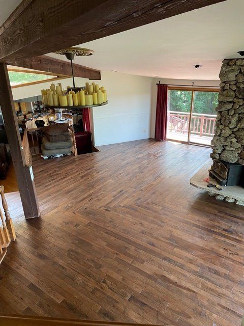 Wooden-floored living room with stone fireplace, chandelier, red curtains, and sliding doors to a deck.